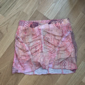 Rosa mönstrad kjol från Tiger Mist - Säljer en kort kjol med inbyggda shorts från Tiger Mist i rosa och beige toner med abstrakt mönster. Kjolen har en tight passform och är tillverkad i ett lätt syntetmaterial. Perfekt för dig som gillar färg och unika plagg!