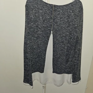 Gråmelerad tröja med vit nederdel från Dorothy Perkins - Säljer en gråmelerad långärmad tröja från Dorothy Perkins med vit nederdel som ger en lager-på-lager-look. Tröjan har rund halsringning och dragkedjedetalj i ryggen. Perfekt för en stilren vardagsoutfit.
