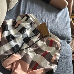 Rutig shorts från Burberry - Säljer ett par snygga shorts från Burberry med klassiskt rutigt mönster i svart, vitt, beige och rött. Shortsen har elastisk midja och snörning för bästa passform. Perfekta för sommaren och riktigt trendiga.
