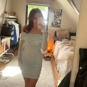 Ljusblå offshoulder klänning - Säljer en ljusblå, tight offshoulder klänning med långa ärmar och rynkade detaljer längs hela klänningen. Den är från Gina tricot och är i storlek XS. Endast använd 1 gång😊💕