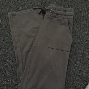 Mörkgrå mjukisbyxor från 157 - Mörkgrå mjukisbyxor från 157 med resår och dragsko i midjan. Byxorna har två sidofickor fram och en bakficka. Perfekta för en avslappnad stil och riktigt sköna att ha på sig. Vänstra benet är uppsprättat