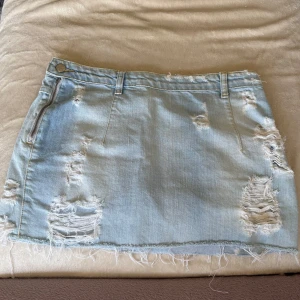 Ljusblå jeanskjol från Perfect Jeans - Säljer en ljusblå jeanskjol från Perfect Jeans med slitna detaljer och rå kant nertill. Kjolen har fickor både fram och bak samt bälteshällor. Perfekt för en avslappnad och trendig look.
