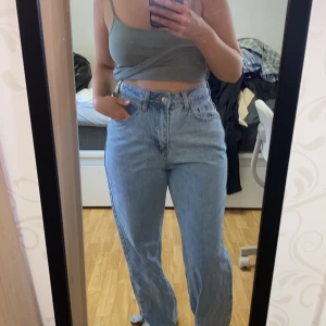 Ljusblå raka jeans - Säljer ett par ljusblå jeans med hög midja och raka ben. Klassisk femficksmodell med knapp och dragkedja framtill. Perfekta till vardags för en avslappnad stil.