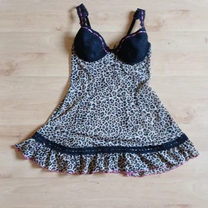 Leopardmönstrad kort klänning med spetsdetaljer - Säljer en kort klänning med leopardmönster och svarta spetsdetaljer upptill. Klänningen har volang nertill och rosa band längs axelbanden. Perfekt för dig som gillar djurmönster och vill sticka ut.