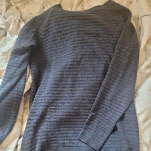 Mörkgrå stickad tröja från Soyaconcept - Mysig mörkgrå stickad tröja från Soyaconcept. Tröjan har en klassisk rund halsringning och långa ärmar. Perfekt för lager-på-lager och enkel att matcha med olika outfits.