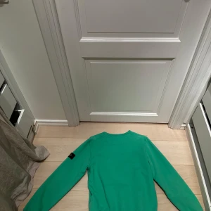 Grön sweatshirt från Stone Island Junior - Säljer en fräsch grön sweatshirt från Stone Island Junior. Tröjan har rund halsringning, långa ärmar och den klassiska Stone Island-loggan på vänster ärm. Perfekt för dig som gillar streetwear och vill sticka ut med en snygg färg.