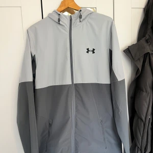 Under Armour Jacka - Extremt fin under Armour windbreaker Grå och ljusgrå färg  Denna modell är slutsåld överallt, detta är jackan utan fickan där vid bröstet Storlek L, passar även M                                               Jackan är exakt som ny, inga defekter  Skicka meddelande vid några funderingar Kolla gärna även in mina andra annonser