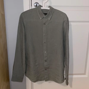 Grön skjorta - Säljer en stilren grå skjorta i 100% linne från Cubus. Den har bara använts ett fåtal gånger och är som ny. Säljer pga att den är för liten.