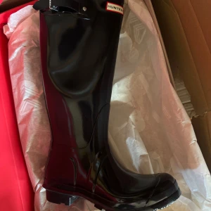 Svarta höga gummistövlar från Hunter - Säljer ett par klassiska svarta gummistövlar från Hunter. Stövlarna är höga med justerbart spänne upptill och har en rund tå samt platt sula. Perfekta för regniga dagar och utomhusaktiviteter.