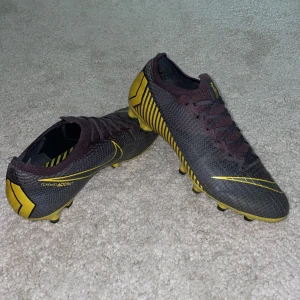 Nike Mercurial Vapor 13 fotbollsskor grå/gul - Säljer ett par NIKE MERCURIAL VAPOR 12 ELITE AG-PRO GAME OVER - GRÅ/GUL fotbollsskor. Skorna har en smal passform och är tillverkade i syntetmaterial med platt sula och rund tå. Perfekta för dig som vill ha snabba och lätta skor på planen. Som ni ser på 4:e bilden så har det blivit hål men inget som jag har haft ont av. Annars mycket bra skick. Kan sänka pris vid snabb affär 💨.  Skicka om du vill ha mer bilder eller andra funderingar! Mvh Axel 