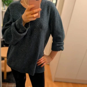 Mörkgrå stickad tröja - Säljer en mörkgrå stickad tröja med rund halsringning och långa ärmar. Tröjan har en klassisk, enkel design och är mjuk och bekväm. Perfekt för lager-på-lager och passar till många olika stilar.