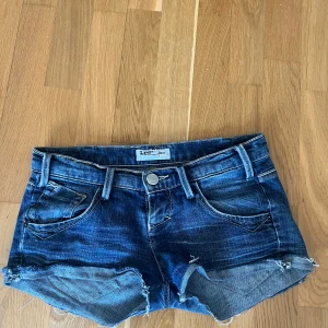 Mörkblå jeansshorts från Lee - Snygga mörkblå jeansshorts från Lee med fransiga benslut och klassiska fem fickor. Shortsen har  och knappgylf, dragkedjan är borta men inget som syns på. Perfekta för varma dagar och enkel att matcha med olika toppar. Skriv till mig, köp inte på köp nu det funkar inte därför jag ej kan koppla mitt bank id till appen!❤️
