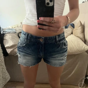 Mörkblå jeansshorts med slitningar - Säljer ett par mörkblå jeansshorts för dom är förstora för mig. Jag har aldrig andvänt dem! De har slitna detaljer, klassisk femficksdesign och råa kanter nertill. Perfekta för varma dagar och skit snygga till allt!