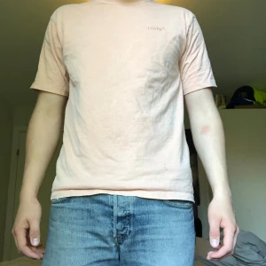 Ljusrosa t-shirt från Levi's - Säljer en ljusrosa t-shirt från Levi's med diskret broderad logga på bröstet. T-shirten har avslappnad passform och är tillverkad i mjuk bomull. Perfekt för en avslappnad stil.