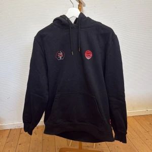Svart Bayern München hoodie Sadio Mané - Svart hoodie från FC Bayern München med Sadio Mané-tryck på ryggen och klubbmärke på bröstet. Tröjan har huva med dragsko och stor magficka framtill. Perfekt för fotbollsälskare som vill visa sitt stöd för laget. L men sitter som M. 