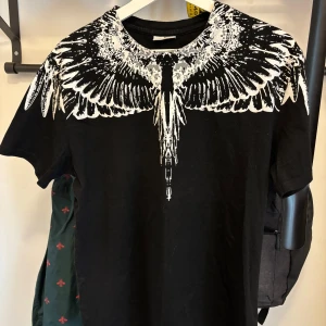 Marcelo Burlon T shirt  - Säljer en svart t-shirt med ett stort vitt fågelmönster som sträcker sig över axlarna och ner på bröstet och ryggen. T-shirten har rund hals och korta ärmar. Perfekt för dig som vill sticka ut med en unik design.