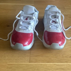 Vita och röda sneakers från Jordan - Säljer ett par vita och röda Jordan sneakers med snörning och rund tå. Skorna har en vit ovandel i syntetmaterial med röda detaljer på sidan och framtill. Sulan är vit med genomskinliga partier undertill. Perfekta för dig som gillar sportig stil.