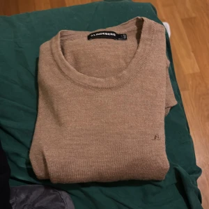 Beige stickad tröja från J.Lindeberg - Säljer en stilren beige stickad tröja från J.Lindeberg. Tröjan har rund halsringning och långa ärmar, perfekt för lager-på-lager. Diskret logga broderad på bröstet. Passar till många olika outfits. Skick 9/10 säljs på grund av för liten då den blev för tight