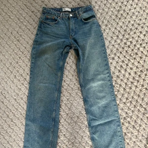 Zara jeans - Säljer ett par klassiska blå jeans från Zara med rak passform och midwaist. Jeansen har fem fickor, knapp och dragkedja framtill samt bälteshällor. Perfekta för en stilren och enkel look.
