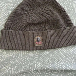 Parajumper jacka - Säljer en brun mössa från Parajumpers med ribbad kant och broderad logotyp framtill. Mössan är stickad och har en klassisk passform som passar till många olika stilar.
