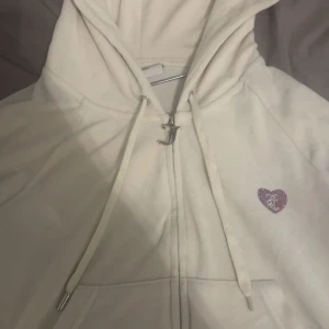 Vit hoodie från Juicy Couture med hjärtdetalj -  PRIS KAN DISKUTERAS MED LÄGRE SUMMA!!!!Säljer en vit hoodie från Juicy Couture i mjukt material. Tröjan har dragkedja, huva och en liten glittrig hjärtdetalj framtill samt ett större hjärtmotiv med text på ryggen. Perfekt för dig som gillar klassisk Y2K-stil! denna är också limetrad edition så är super svår o få tag o 