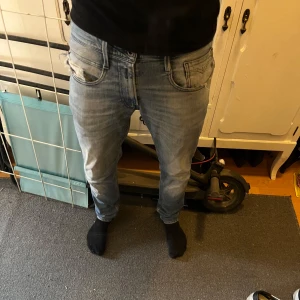 Replay jeans - Säljer ett par ljusblå Replay jeans med klassisk femficksdesign och snygga slitningar. Jeansen har raka ben och normal passform, med tydliga Replay-detaljer på bakfickan och patch på linningen. 