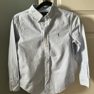 Randig Ralph Lauren skjorta - Säljer en stilren blå vit skjorta med ett märke Ralph lauren märke på bröstet. Storleken är 12 år och säljer pga av att den är för liten