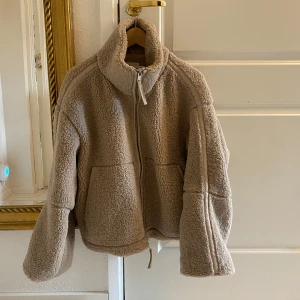 Beige teddyjacka med dragkedja från H&M - Mysig beige teddyjacka med hög krage och dragkedja framtill. Jackan har en oversized passform och är tillverkad i ett fluffigt teddy-material som håller dig varm. Perfekt för kyliga dagar och enkel att matcha med olika outfits.  Den är använd ett fåtal gånger endast och har inga defekter. Storlek M. 