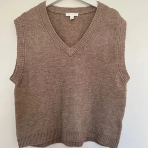 Beige stickad väst med v-ringning - Mysig beige stickad väst med v-ringad hals och ribbade kanter. Perfekt att bära över en skjorta eller t-shirt för en avslappnad men stilren look.