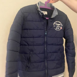 Mörkblå pufferjacka  - Säljer en mörkblå pufferjacka från Hampton Republic med dragkedja och ståkrage. Perfekt för kyligare dagar.