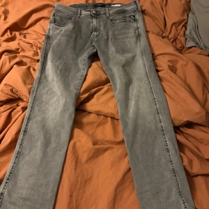 Grå Replay Hyperflex jeans - Säljer ett par grå jeans från Replay Hyperflex-serien. De har klassisk femficksdesign, knappgylf och raka ben. Jeansen är i stretchigt material som ger extra komfort och rörelsefrihet. Perfekta för dig som vill ha en stilren och avslappnad look.