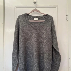 Grå stickad tröja med v-ringning från Vila - Mysig grå stickad tröja från Vila med v-ringad hals. Perfekt för lager-på-lager och passar till många olika outfits. Tröjan har långa ärmar och ribbade muddar vid ärmslut och nederkant.