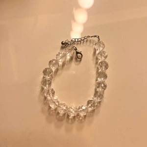 Armband med transparenta pärlor - Säljer ett stilrent armband med stora, transparenta pärlor och justerbart metallspänne. Perfekt accessoar för att ge en glittrig touch till din outfit. Passar de flesta handleder tack vare den flexibla kedjan. Pärlorna är äkta bergartskristall