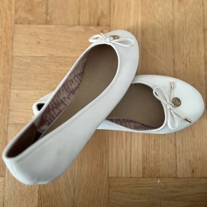 Vita ballerinaskor - Supersöta vita ballerinaskor från DinSko med dekorativ rosett framtill och små gulddetaljer. Skorna har rund tå och är helt perfekta under en somrig klänning! Fråga för fler bilder! 🤍