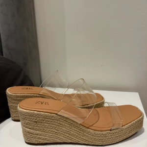 Zara sandaler  - Säljer ett par snygga sandaler från Zara med hög platåsula i rep och två breda transparenta remmar. Skorna har öppen tå och fyrkantig form framtill, perfekta för sommaren. Storlek 40, priset kan diskuteras! 🥰
