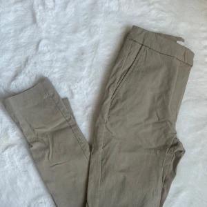 Beige kostymbyxor från Mango - Snygga beige kostymbyxor från Mango . Perfekta för en stilren look och enkla att matcha med olika toppar. Byxorna är varken höga eller låga i midjan. Stretchiga. Använda 1 gång.