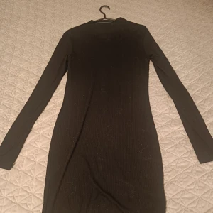 Svart ribbad långärmad klänning - En svart, ribbad klänning med lång ärm och rund halsringning. Klänningen har en tight passform och är perfekt för dig som gillar en enkel men stilren look.