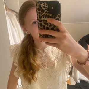 Vit spetsblus med volangärmar - Säljer en söt vit blus med spets och volangdetaljer på ärmarna. Blusen har ett vackert mönster.. Den är kortärmad och har rund halsringning💕