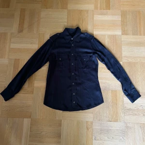 Limitato Skjorta - Säljer en svart skjorta från Limitato med unikt fototryck på ryggen. Skjortan har långa ärmar, klassisk krage och knäppning framtill samt två bröstfickor med lock. Perfekt till sommaren. Skjortan är köpt på Nk Göteborg och är knappt använd pga fel Strlk.