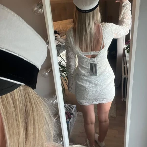 Vit spetsklänning  - Superfin vit spetsklänning med långärmade, lätt utsvängda ärmar och öppen rygg. Kort modell med figurnära passform och vackert spetsmönster över hela klänningen. Perfekt för student. Vi på bilderna bär i vanliga fall storlek Xs/S och är ca 165 cm långa. Klänningen är storlek M 🌸