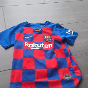 FC Barcelona Messi 10 matchtröja - Säljer en FC Barcelona fotbollströja från Nike med Messi 10-tryck på ryggen. Tröjan har rödblått rutmönster, klubbmärke på bröstet och Rakuten som sponsor. Kortärmad modell i lätt material, perfekt för fotboll eller support.