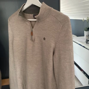 Beige merinoullströja med halv dragkedja från Morris - Säljer en stilren beige tröja från Morris i 100% merinoull. Tröjan har halv dragkedja med läderdetalj och diskret broderad logga på bröstet. Perfekt för lager-på-lager och passar till många olika outfits. Storleken var XL men krymptes i tvätten till mellan XS och S.