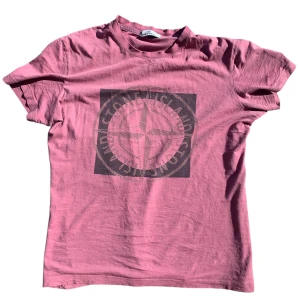 Rosa t-shirt från Stone Island - Säljer en rosa t-shirt från Stone Island med stort svart tryck på bröstet och logga i nacken. T-shirten har rund hals och korta ärmar. Perfekt för dig som gillar streetwear och vill sticka ut med en snygg färg.