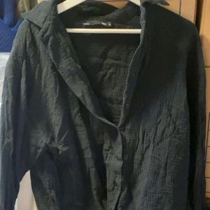Svart skjorta i bomull - Säljer en svart skjorta  i mjukt, krinklat bomullstyg. Skjortan har klassisk krage, knäppning framtill och långa ärmar. Perfekt för en avslappnad och stilren look.