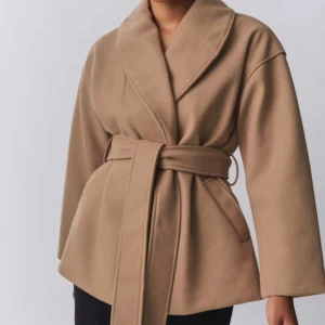 Beige kappa med bälte och bred krage - Säljer en beige kappa med bred sjalkrage och knytskärp i midjan. Jackan har lång ärm och två sidofickor. Perfekt för dig som gillar en stilren och enkel look.Jackan är från Gina tricot.helt ny med lappar 