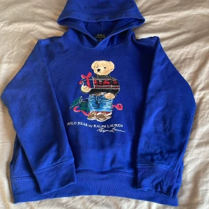 Blå hoodie med björn från Polo Ralph Lauren  - Säljer en blå Polo Ralph Lauren hoodie. En blå stilren hoodie med ett tryck därframme. Ny pris 1500 säljer för 600 kr pris går att diskutera om, skicka vid funderingar. 
