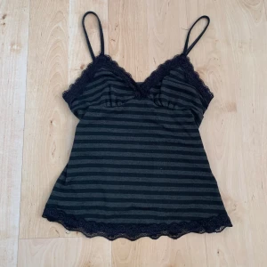 Svart och grå randig linnetopp med spets - Säljer en svart och grå randig linnetopp i storlek S med tunna axelband och fina spetsdetaljer vid byst och nederkant. Toppen är ärmlös och har en mjuk, bekväm passform. Perfekt för sommaren eller som ett lagerplagg. Bysten är för liten för mig som har C kupa.