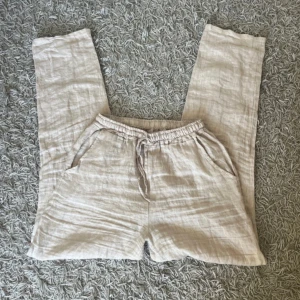 Beige linnebyxor Design by si  - Snygga och luftiga beige linnebyxor med resår i midjan. Raka ben och sidofickor, perfekta för varma dagar. 100% linne. Inga tecken på användning, fint skick!  