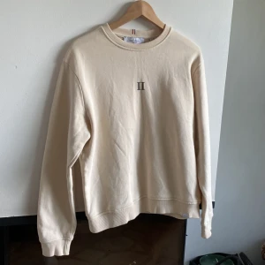 Beige sweatshirt från Les Deux - Säljer en stilren beige sweatshirt från Les Deux med diskret broderad logga på bröstet. Tröjan har rund halsringning och långa ärmar. Perfekt för en avslappnad stil