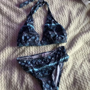 Mönstrad blå bikini från Panos Emporio - Säljer en snygg blå bikini från Panos Emporio med mönster i olika blå nyanser och vita detaljer. Bikinin har halterneck med knyt i nacken och klassiska bikinitrosor. Materialet är mjukt och stretchigt, perfekt för stranden eller poolen. aldrig använda bara testade (med underkläder under) säljer för den inte passade men aldrig orkar lämna tillbaka så säljer istället 